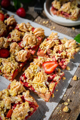 Strawberry and rhubarb meringue crumble squares on baking paper on old wooden table.