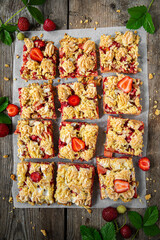 Strawberry and rhubarb meringue crumble squares on baking paper on old wooden table.