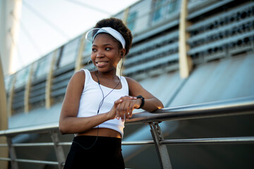 Young african woman training outdoors. Female runner using smart watch