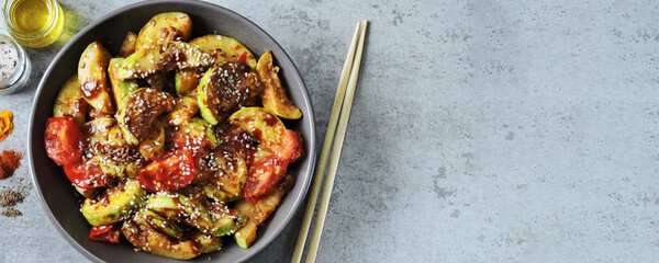 Fried zucchini slices in Asian style in a bowl with sesame seeds and vegetables.