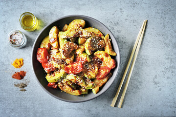 Fried zucchini slices in Asian style in a bowl with sesame seeds and vegetables.