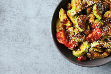 Fried zucchini slices in Asian style in a bowl with sesame seeds and vegetables.