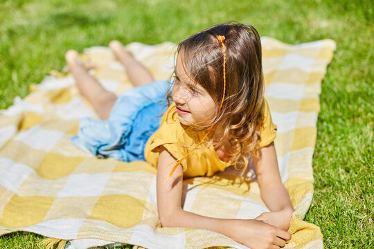 Child lying on the blanket, on the grass in the sun day, little girl take sunbathes on backyard