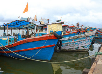 orange and blue fishing motor boats lined up in a fishing sea harbor in the evening with puffy clouds in the sky