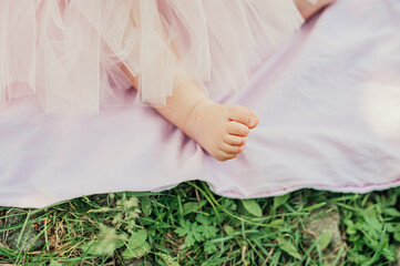 pretty little naked feet of girl on pink plaid in lush pink tulle skirt on green lawn. selective...