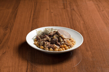 Asian cuisine Uzbek food Nukhot shurak, stewed chickpeas with meat, in a white plate with onions and horse meat sausage on the table
