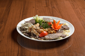 Asian cuisine Uzbek food Beshbarmak, pieces of boiled dough with boiled meat and broth on a plate, decorated with horse meat sausage and chickpeas on the table
