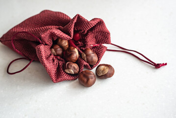 Elegant small sack with ropes and pile of scattered dry brown chestnuts lie on light grey stone table in studio close view - obrazy, fototapety, plakaty