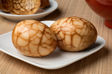 Pair of traditional Chinese herbal tea eggs on a plate as snack food close up and eggshell in the background 