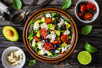Fresh vegetable salad with mozzarella, tomatoes, avocado, lettuce, black olives and onion on wooden table
