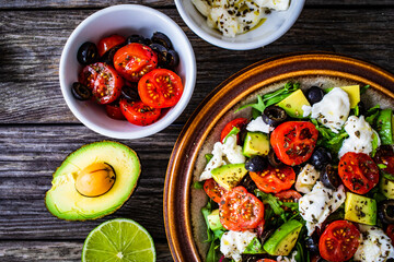 Fresh vegetable salad with mozzarella, tomatoes, avocado, lettuce, black olives and onion on wooden table
