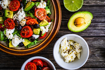 Fresh vegetable salad with mozzarella, tomatoes, avocado, lettuce, black olives and onion on wooden table
