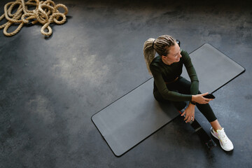 Young sportswoman with prosthesis using cellphone while sitting on mat