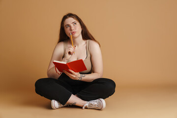 Pensive young plus size woman holding pencil and diary