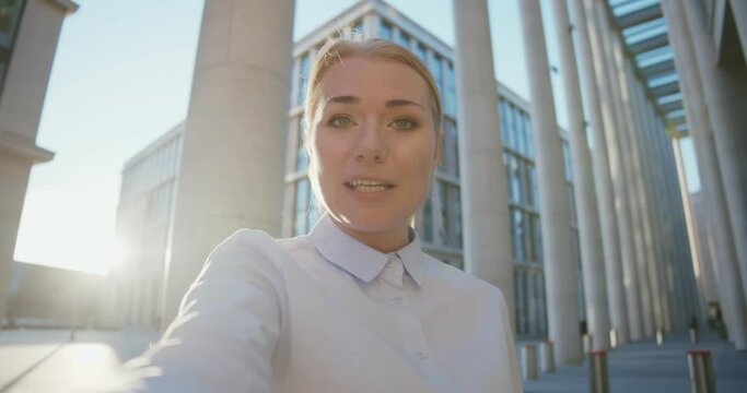 Young beautiful businesswoman having video conference outside office building
