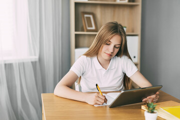 An attractive student is studying an online course and taking notes while preparing for the exam with a tablet. The concept of education and upbringing, preparation for exams