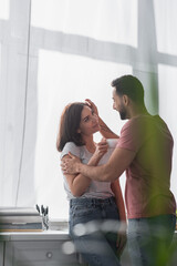 smiling young man gently touching girlfriend with white coffee cup in modern kitchen