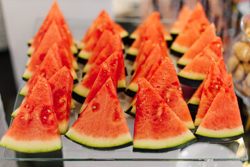 Slices of sliced watermelon are lying on glass table of fruit buffet. Healthy food. Natural desserts. Lifestyle. Freshness and coolness.