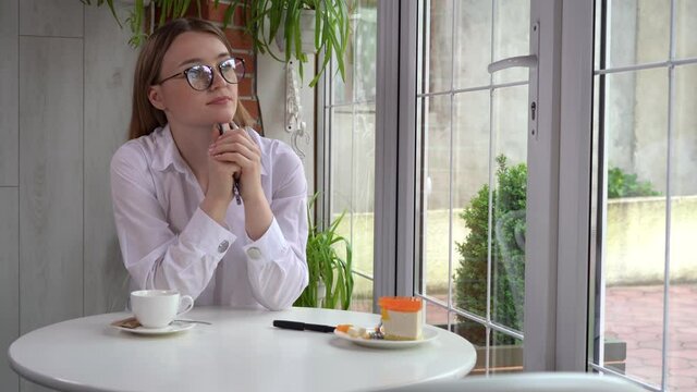 pensive blonde woman sits at a table in a cafe and holds her smartphone in her hands, looks around.