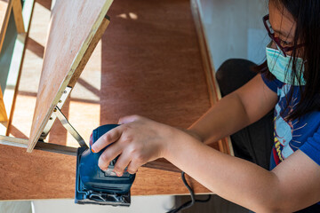 A young girl is hand sanding wood with a machine in the craftsman workshop.