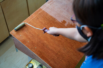 Hand holding roller and applying polyurethane on the wooden board by a young girl.