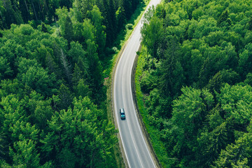 Aerial view of curved country road with cars and green summer woods.
