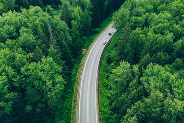 Aerial view of curved country road with cars and green summer woods.