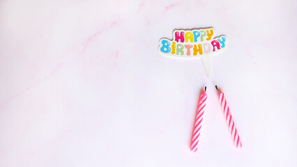 Flat lay of two birthday candles with a paper speech bubble on top, written Happy Birthday in colorful letters. With pink marble background.