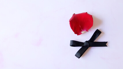 A single red rose petal, with a black ribbon bow below it. On pink marble background and copy space on the left.
