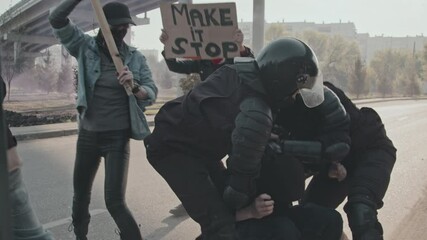 Slowmo tracking shot of two riot police officers in full gear running up to male protester and arresting him
