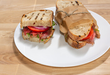 Two sandwiches with slices of beef, tomatoes, green salad and onions on a white plate against the background of a wooden table