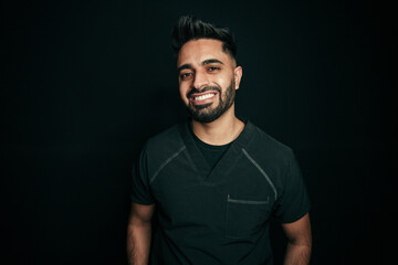 Mixed race male dentist smiling for head shot portrait standing against black backdrop