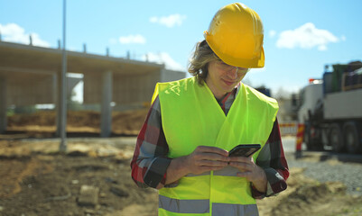 Builder writes sms on smartphone at construction site.