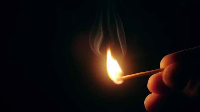 Slow motion burning match in hands in darkness. Close up male hand holding burning match in pitch darkness