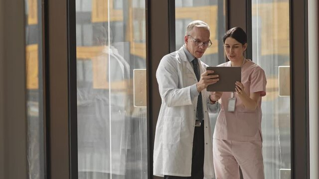 Medium slowmo of two contemporary male and female doctors looking at digital tablet display examining radiograph of patient thinking about diagnosis