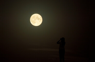 Fototapeta na wymiar A young girl watches a beautiful huge moon in the night sky