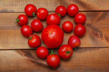 Fototapeta na wymiar A bunch of fresh ripe red tomatoes in the form of a heart on a wooden background. Close-up.