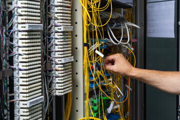 Hands of a technician crossing a telecommunication panel cable in a rack