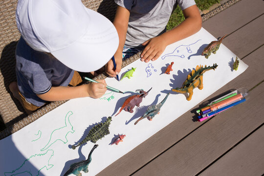 Two unrecognizable preschoolers draw contrasting shadows from toy dinosaurs with felt-tip pen. creative ideas for children's creativity. Interesting activities for children at home and in kindergarten