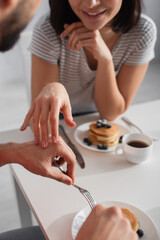 partial view of young woman touching hand of boyfriend eating breakfast in kitchen