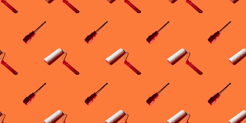 Paint rollers and screwdrivers on an orange background, pattern, hard shadows. Construction tools, repairs. Background for the design.
