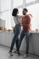 happy young woman hugging boyfriend with hands on shoulders in kitchen