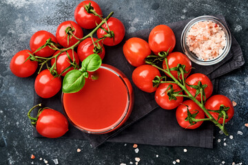 Glass of fresh tomato juice, salt, basil and tomatoes on black plate on old black background. Top view with copy space.
