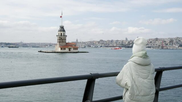 Tourist woman looking to Maiden Tower in Bosporus on observation deck in Istanbul city, Turkey. Young female traveler sightseeing to Kiz Kulesi Tower