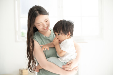 赤ちゃんを白い綺麗な部屋で抱っこする笑顔の美人ママのズーム コピースペースあり