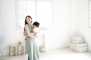赤ちゃんを白い綺麗な部屋で抱っこする笑顔の美人ママ1...
