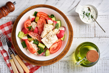 Radish, cucumber, tomato, pepper and feta cheese with spices pepper and olive oil in white bowl on grey slate, stone or concrete background. Healthy food concept. Top view.