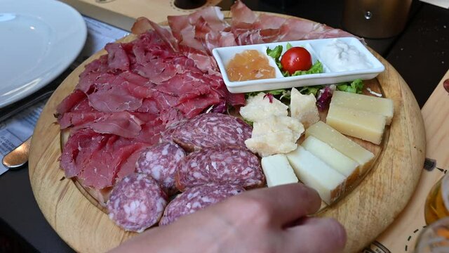 An appetizing platter of cold cuts and assorted cheeses with Trentino specialties such as speck, to accompany sauces. One hand grabs a piece of cheese. Concept of typical and healthy Italian food.