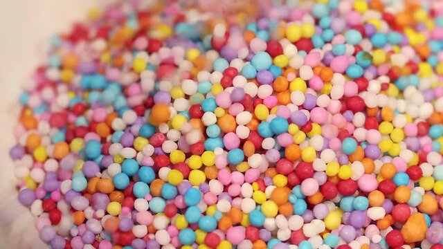 Macro close up of colored candy sprinkles falling into a white bowl