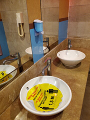 Bathroom interior with social distancing sign inside sink forbidding to use it due to covid restriction. Yellow sticker in Turkish, English, German, Russian. Text - keep social distance